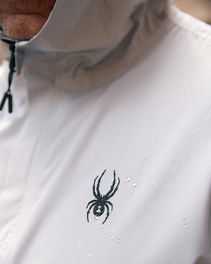 Close-up of a white hoodie with a black spider logo on the chest.