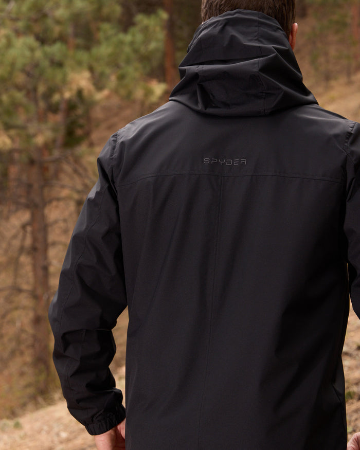Person wearing a black jacket with 'Spyder' branding in a forest setting