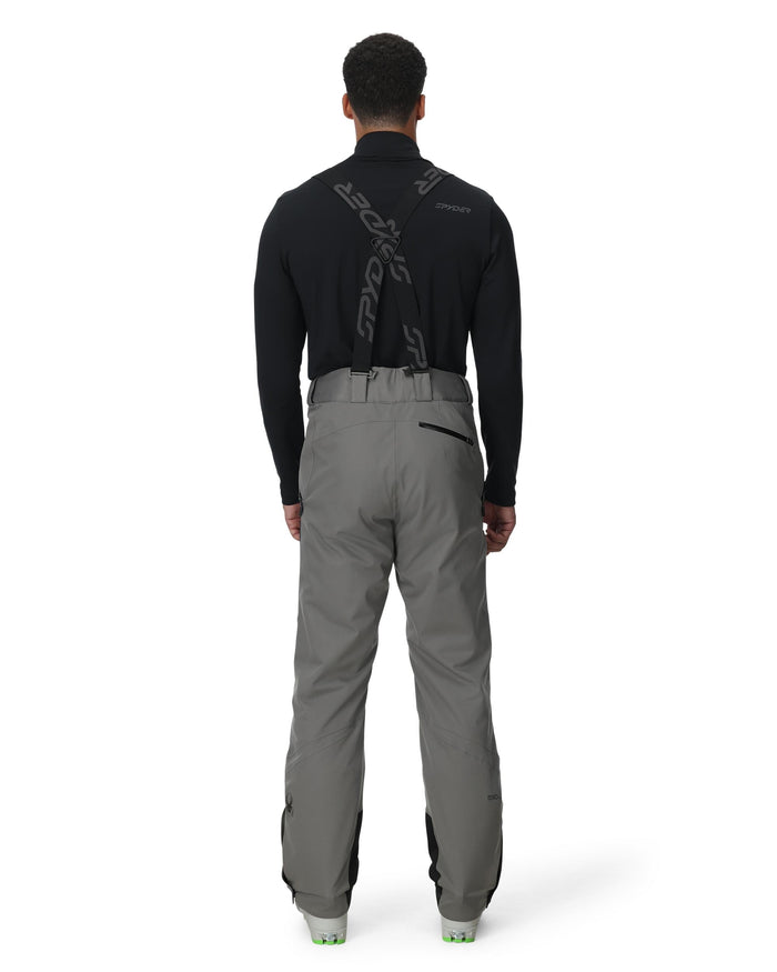 Person wearing a black jacket and gray pants on a white background