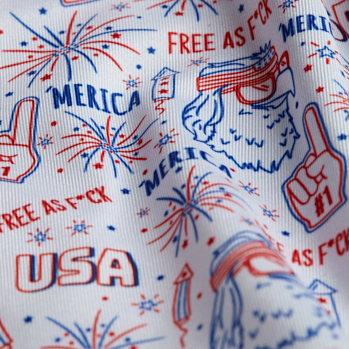 A close-up of the 'Merica - Polo: white fabric with red and blue prints—fireworks, “USA,” #1 fingers, a bearded man in sunglasses and headband. Bold “MERICA” and “FREE AS F*CK.” Athletic fit, moisture wicking.
