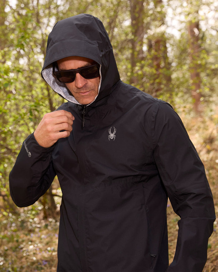 Man wearing a black jacket with a hood in a forest setting