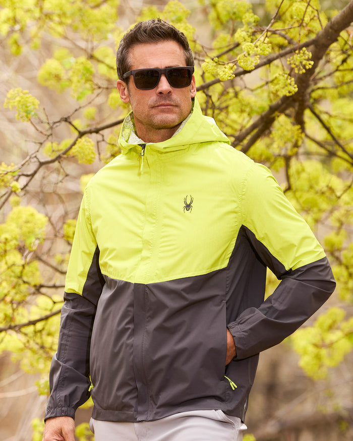 Man wearing a two-tone jacket with a logo in front of green foliage