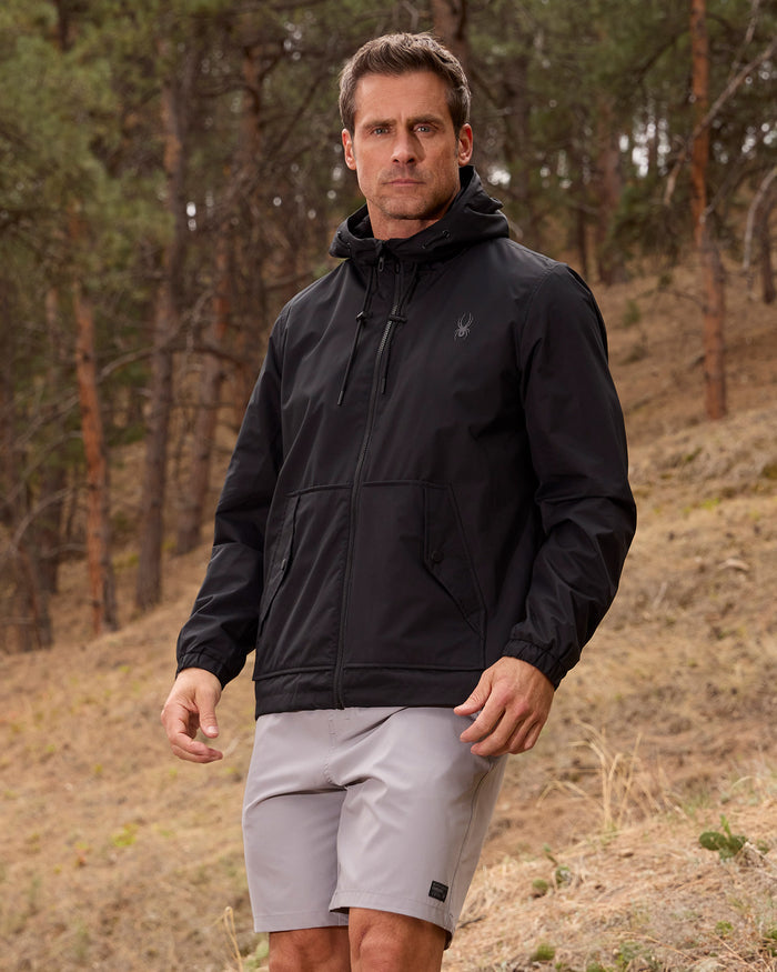 Man wearing a black jacket and gray shorts standing in a forested area