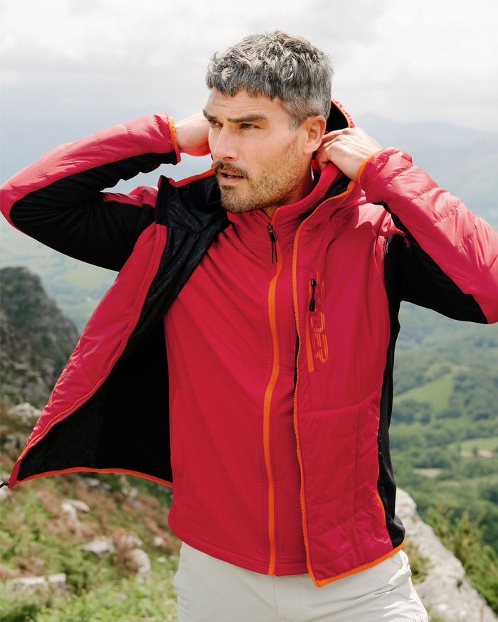 Man wearing a red and black jacket with orange accents in a mountainous landscape