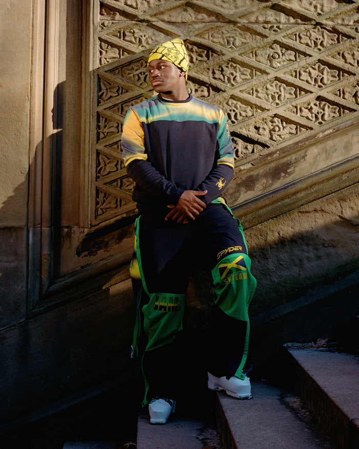 Person wearing a colorful outfit with green, yellow, and blue patterns sitting on steps.