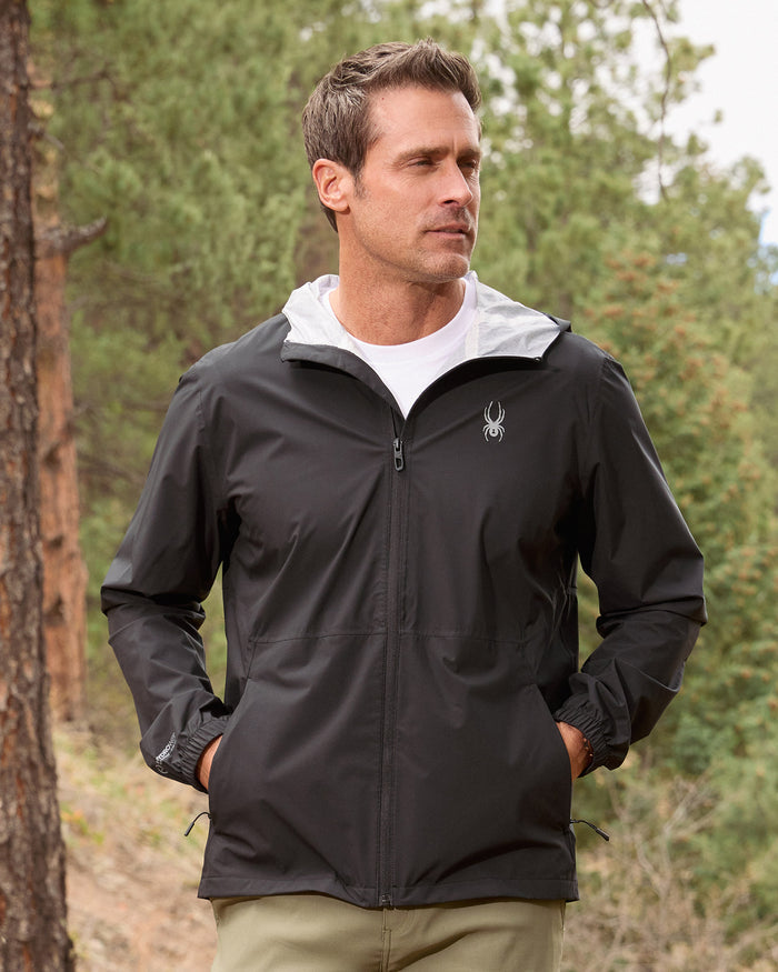 Man wearing a black jacket with a white hood in a forest setting