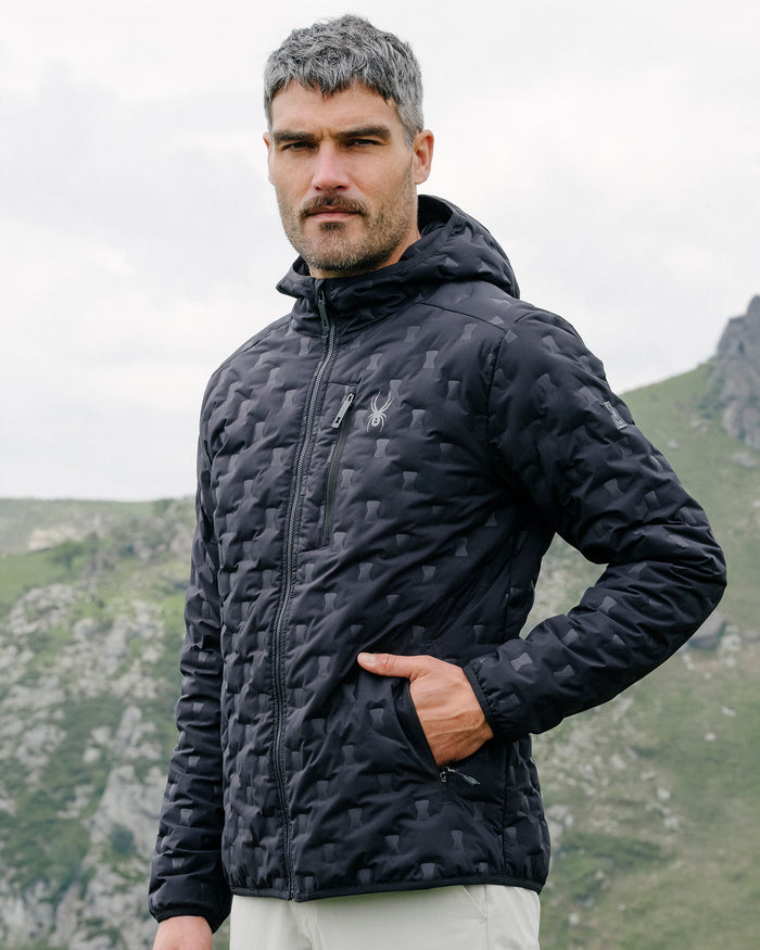 Man wearing a black quilted jacket with a mountainous landscape in the background