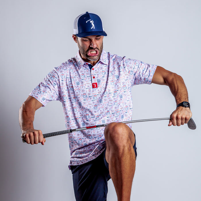 A man in an athletic fit 'Merica - Polo, blue shorts, and a blue-and-white cap grimaces angrily as he tries to snap a golf club over his knee. His watch is visible on his left wrist against a plain light gray background.